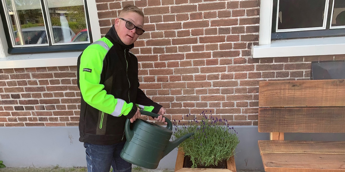 een jongen met bril geeft met een gieter een lavendelplant water