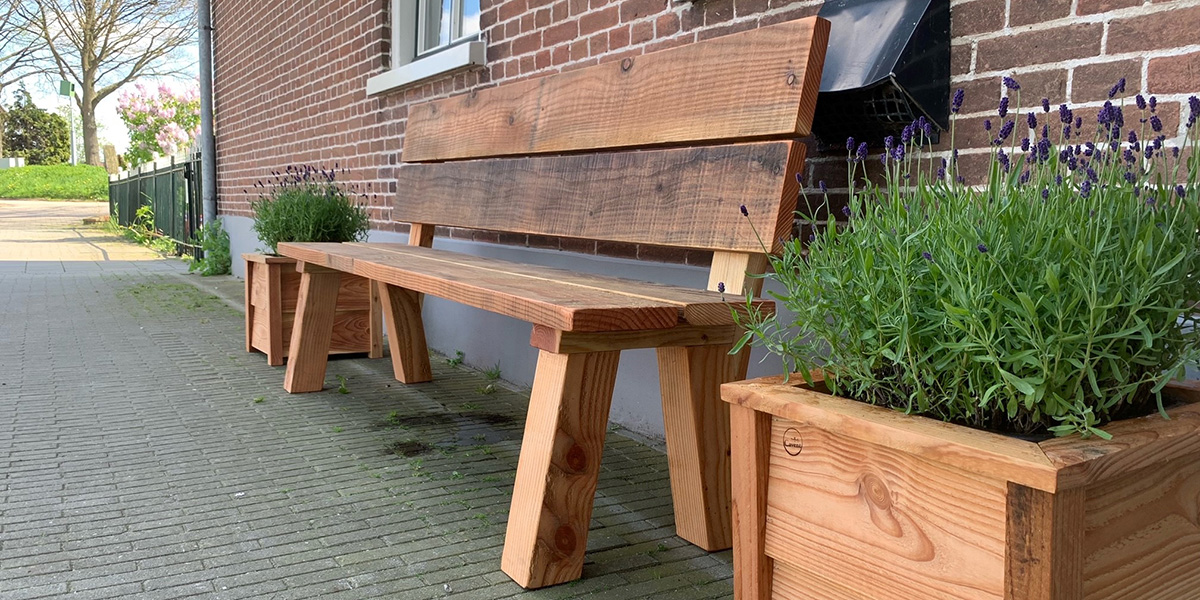 een robuuste houten tuinbank met aan elke kant een houten plantenbak met een lavendelplant