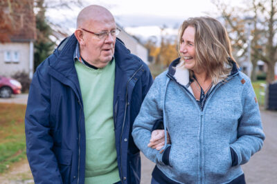 oudere man en jongere vrouw lopen gearmd en lachend naast elkaar